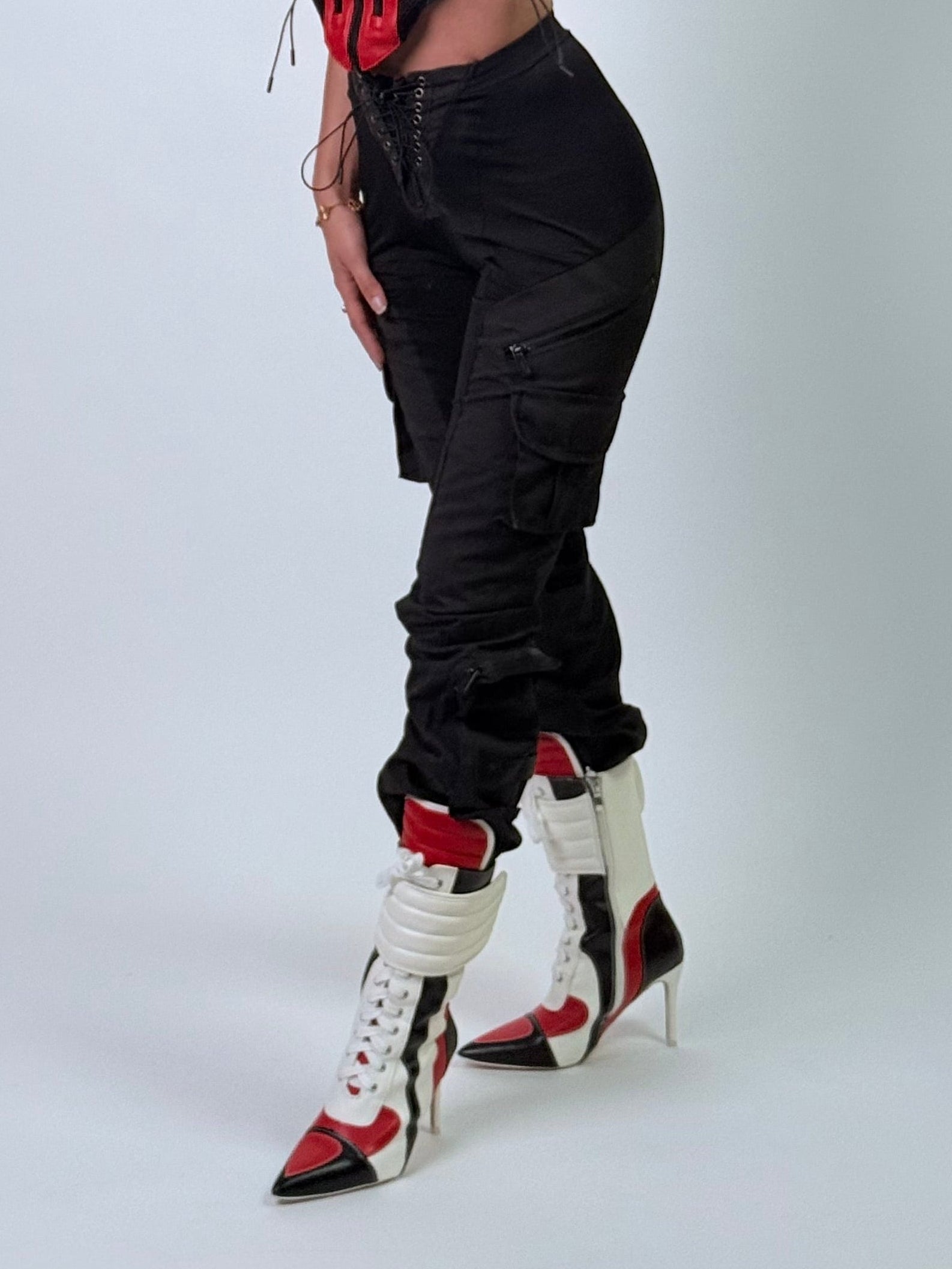 Person wearing a red corset, black pants, and white high-heeled boots on a light gray background