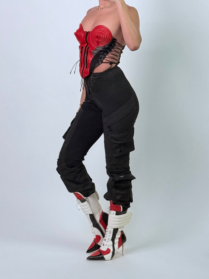 Person wearing a red corset top and black pants with white and black shoes on a white background